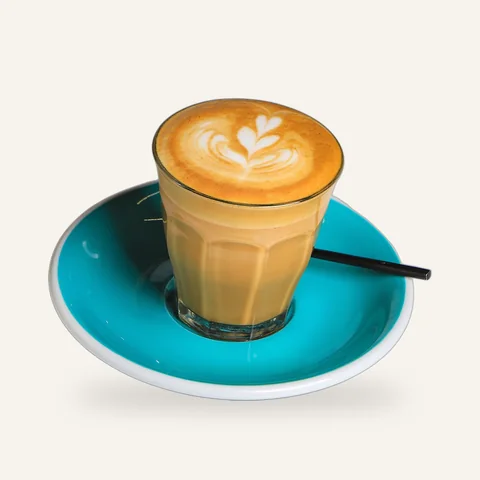 Flat white in a glass on a teal saucer